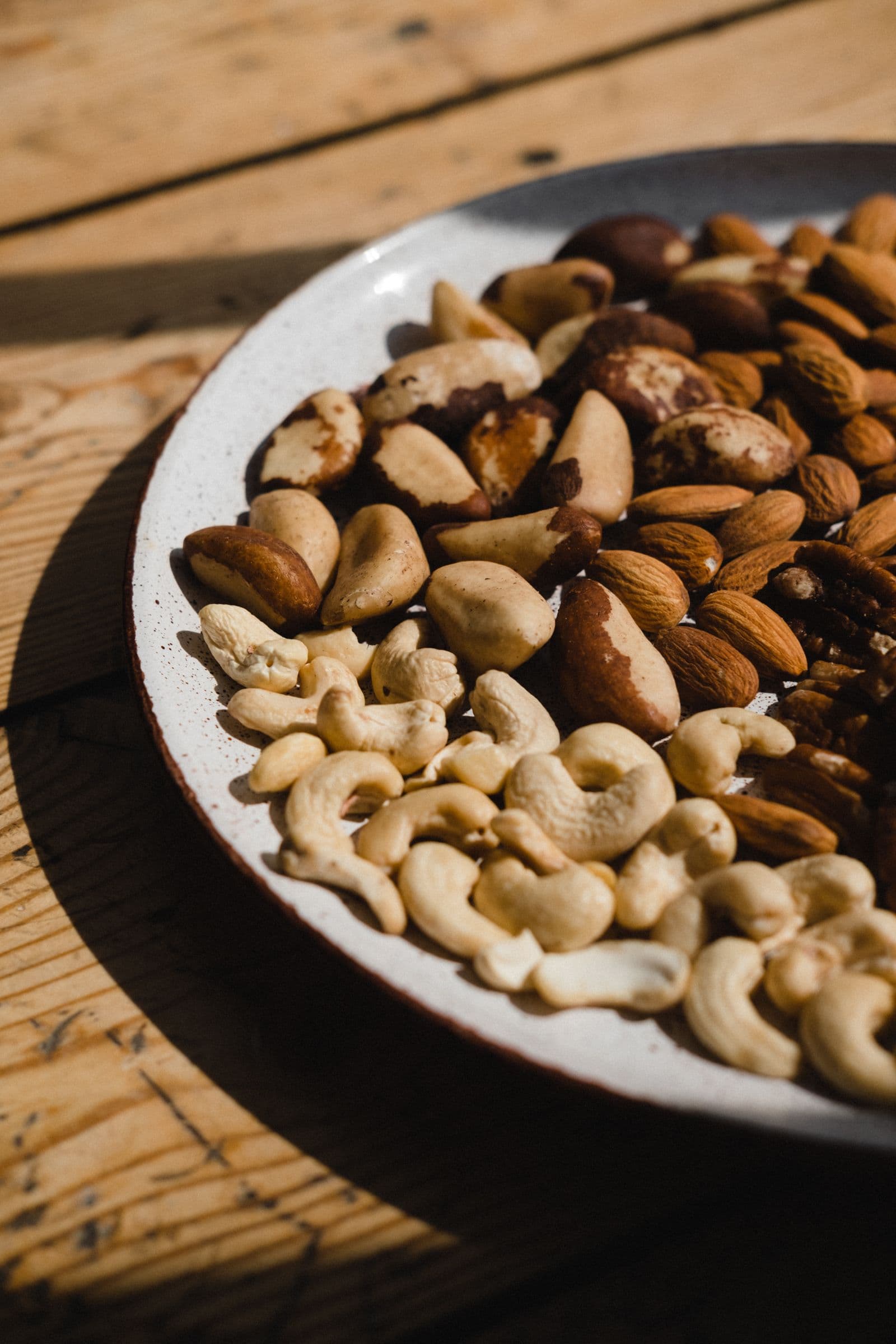 A plate of premium mixed nuts - almonds, cashews and Brazil nuts - in warm natural light